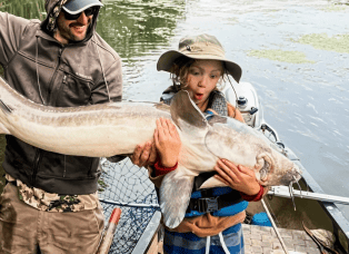 A thrilled Wisconsin youth and father holding a giant lake sturgeon on a boat – Fathead Fran’s rod and reel repair WI.