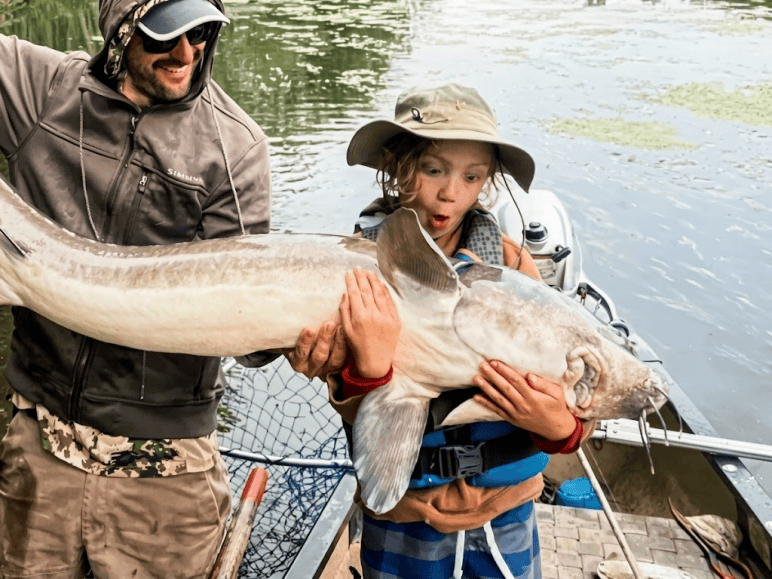 A thrilled Wisconsin youth and father holding a giant lake sturgeon on a boat – Fathead Fran’s rod and reel repair WI.